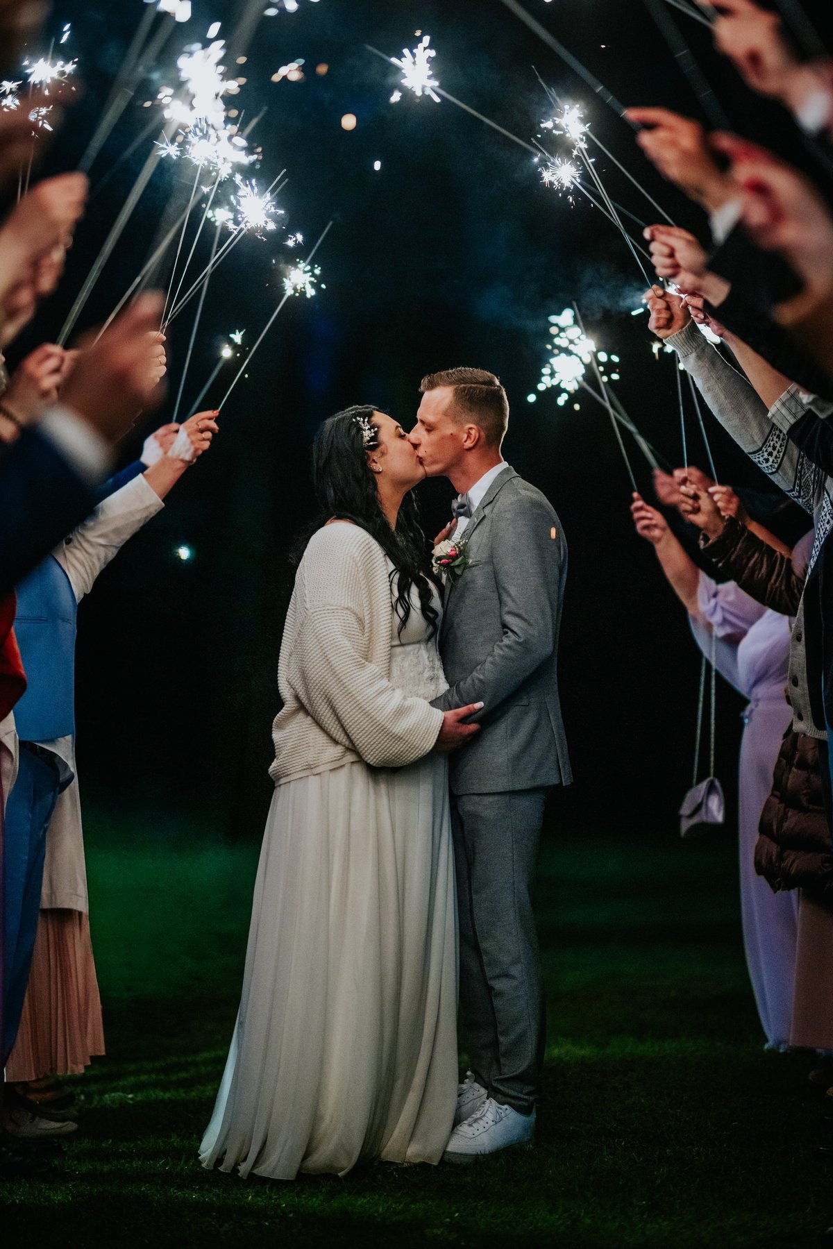 Couple embraces in a heartfelt kiss as guests celebrate with sparklers at Keys Hotel Mbokomu Moshi wedding