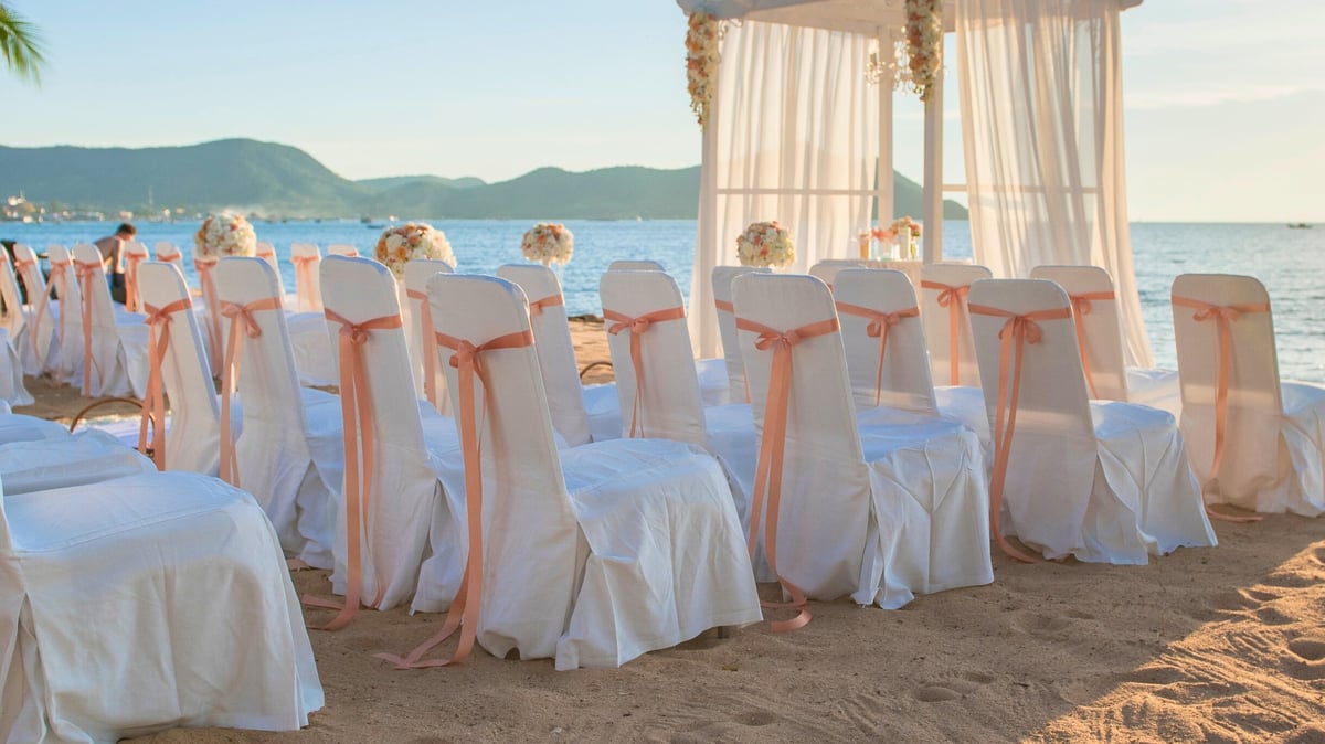 White chairs with pink sashes on sandy beach for outdoor wedding ceremony at Honey Badger Lodge Moshi