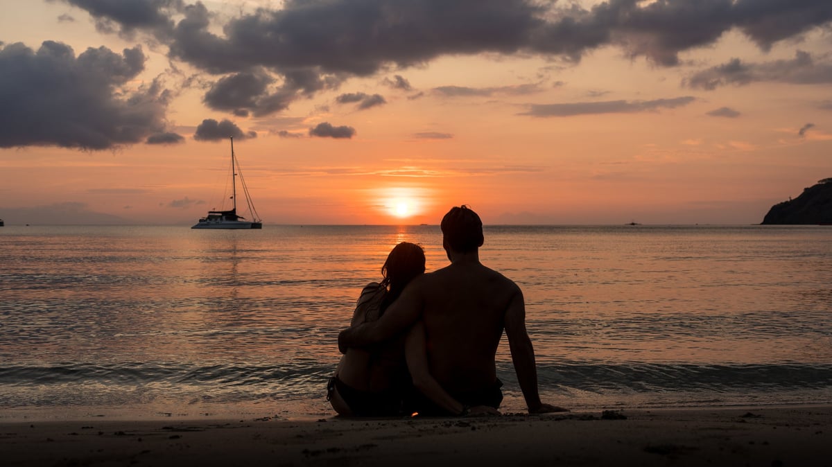 Couple sitting on the sand of a beach at sunset