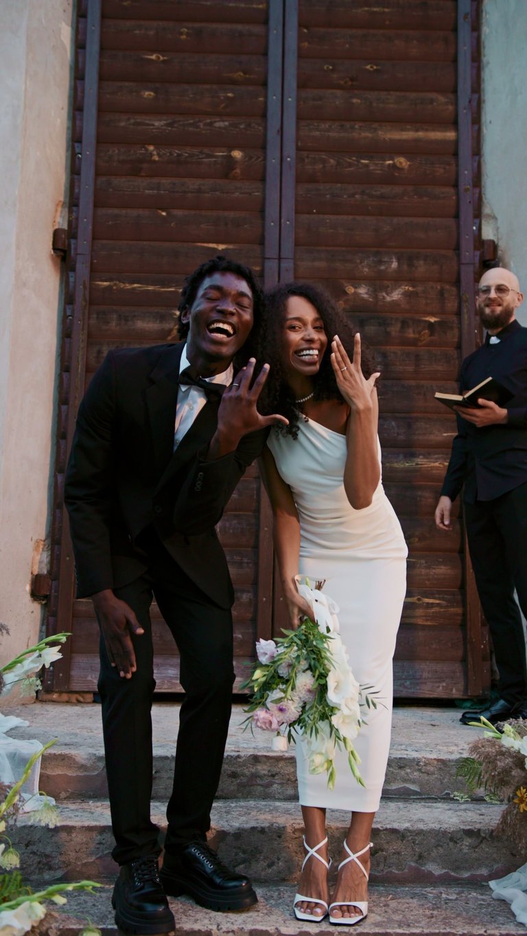 Bride and groom rejoicing showing wedding rings and kissing standing before priest at outdoor Lake Tanganyika Kigoma wedding ceremony