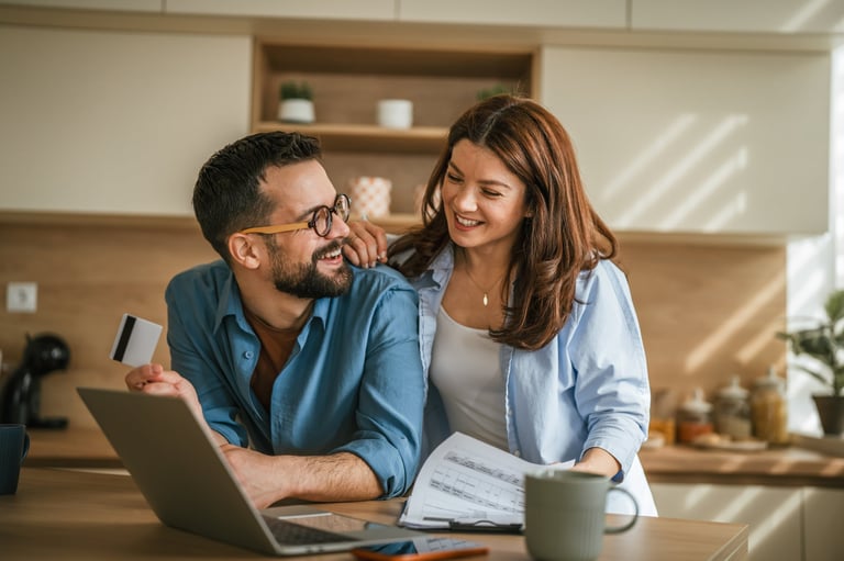 Happy couple calculating expenses, paying bills, and making online purchases with credit card and laptop, focusing on budget planning and financial management at home — Send-Off to Wedding Gap Planner Tanzania