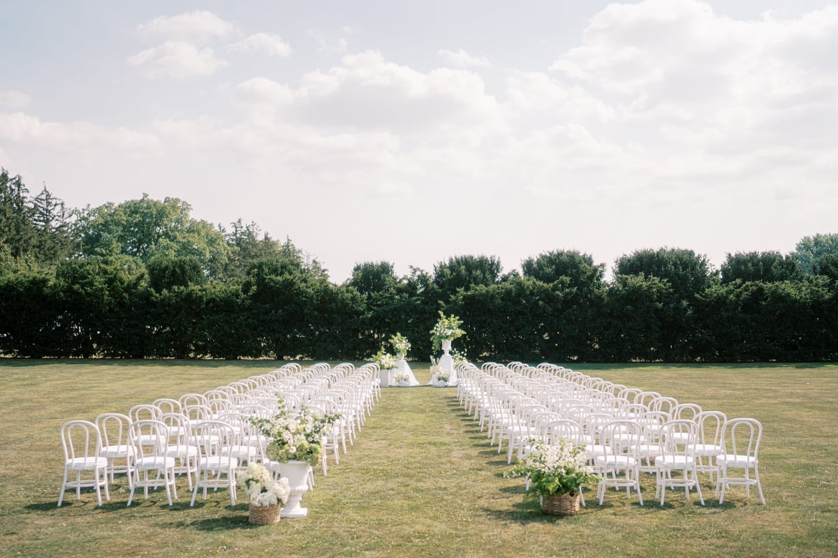Wide outdoor wedding aisle lined with white chairs leading to floral arch at Materuni Waterfalls Moshi