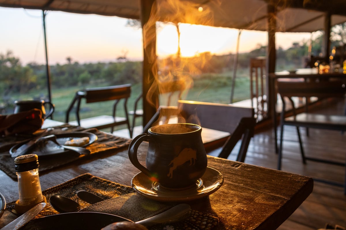 Steaming hot coffee on a breakfast table at sunrise in a luxury Serengeti tented camp
