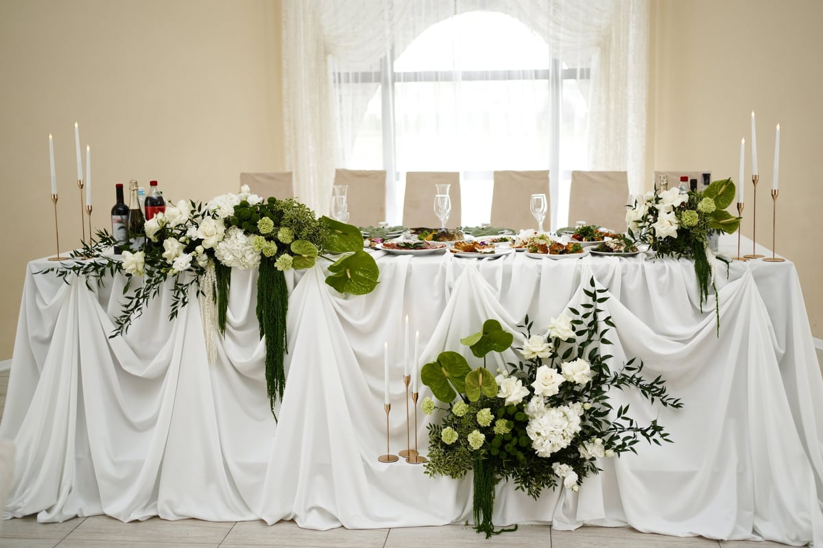 Beautifully decorated wedding head table at New Dodoma Hotel with white drapery, floral arrangements and festive setting