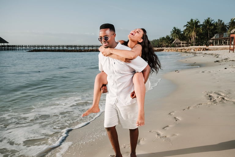 Groom carrying bride in white wedding dress on tropical Zanzibar beach with Indian Ocean pier and palm trees luxury Tanzania wedding photography