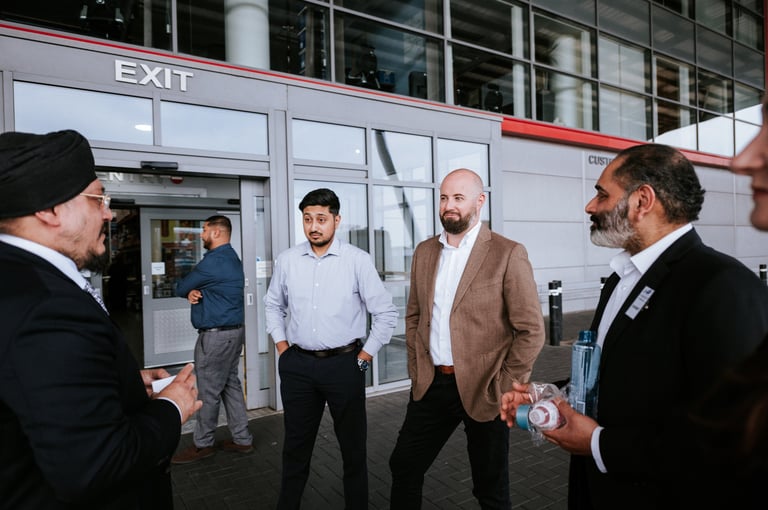 Corporate event photography — group of business professionals in suits standing outside modern building exit door having a discussion, Royal Wedding Cinema & Photography Tanzania