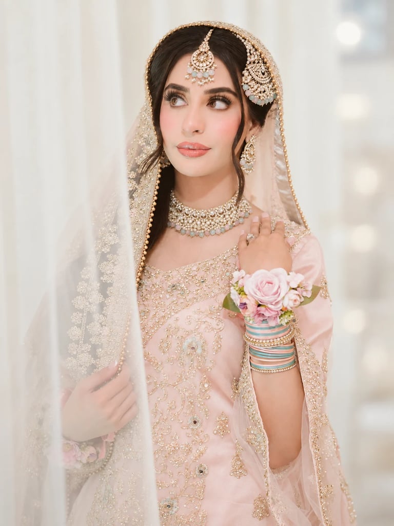 Woman in ornate pink beaded wedding dress with matching veil, jewelry, and floral wrist corsage in formal bridal portrait