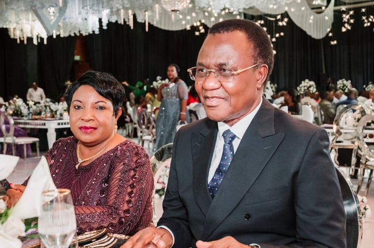 A man in a dark suit and woman in a burgundy dress seated at a formal event table with elegant decorations and guests in background