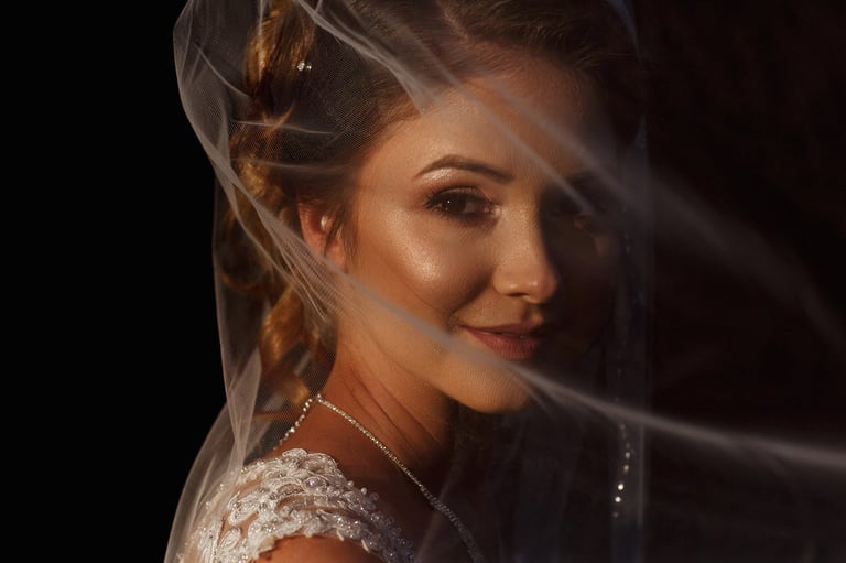 Woman in white lace dress and veil looking over shoulder against dark background