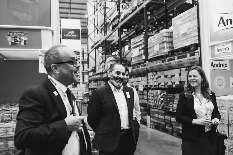 Corporate industrial photography — three business professionals in formal attire standing in warehouse supply facility, Dar es Salaam Tanzania
