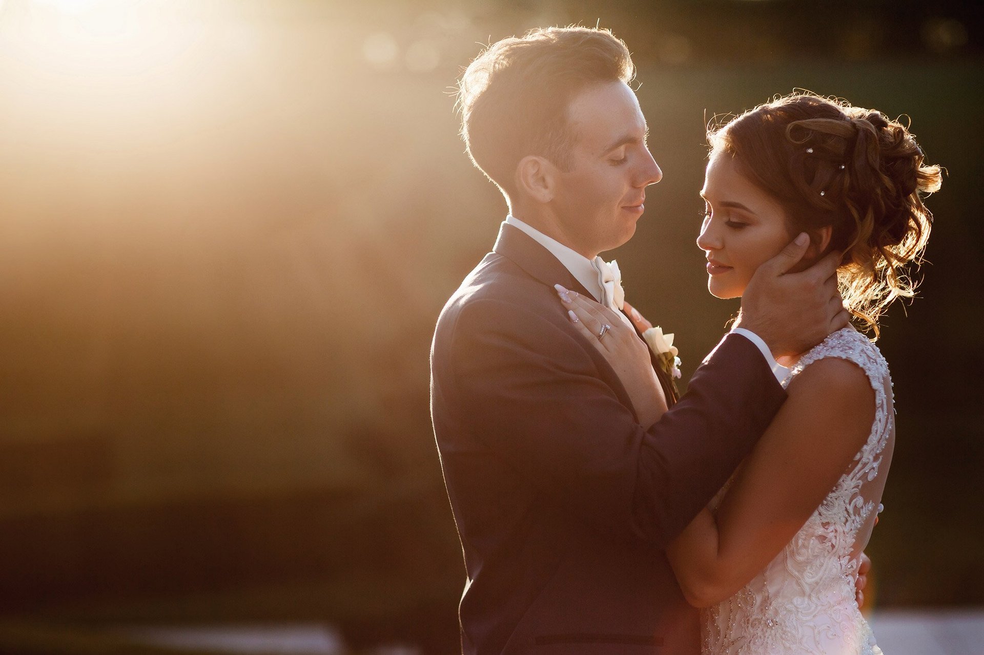 Groom and bride embracing outdoors at sunset, backlit golden light, romantic wedding moment