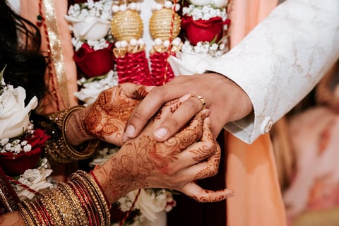Close-up of bride and grooms hands displaying wedding rings during traditional Indian wedding ceremony with henna and floral decorations visible