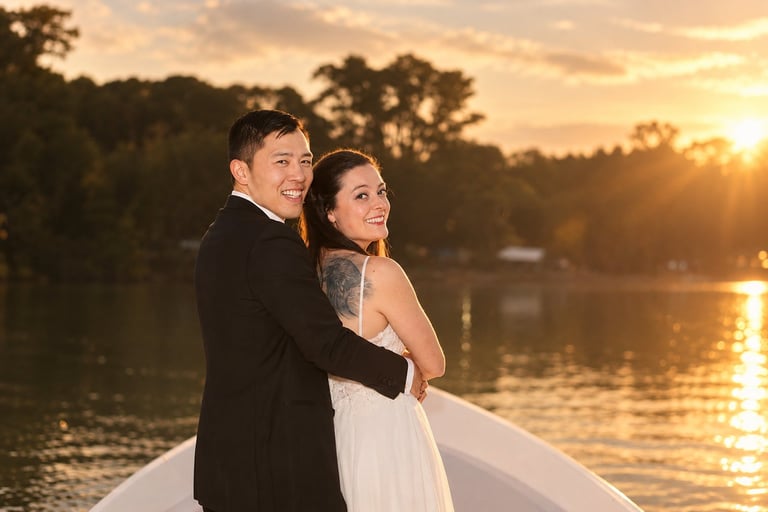 Bride and groom posing together on a boat at sunset with golden water and trees in the background