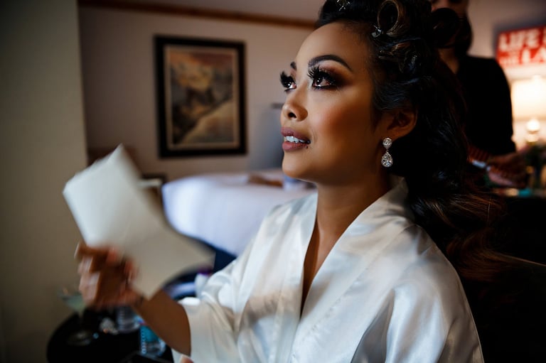Bride in white robe applying makeup in a bedroom, wedding preparation moment in Tanzania