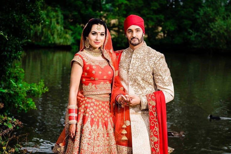 Indian couple in traditional wedding attire posing by a riverside with green foliage background