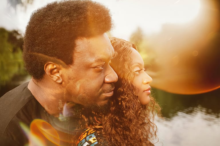 Man and woman smiling outdoors at sunset, with a lake visible in the blurred background