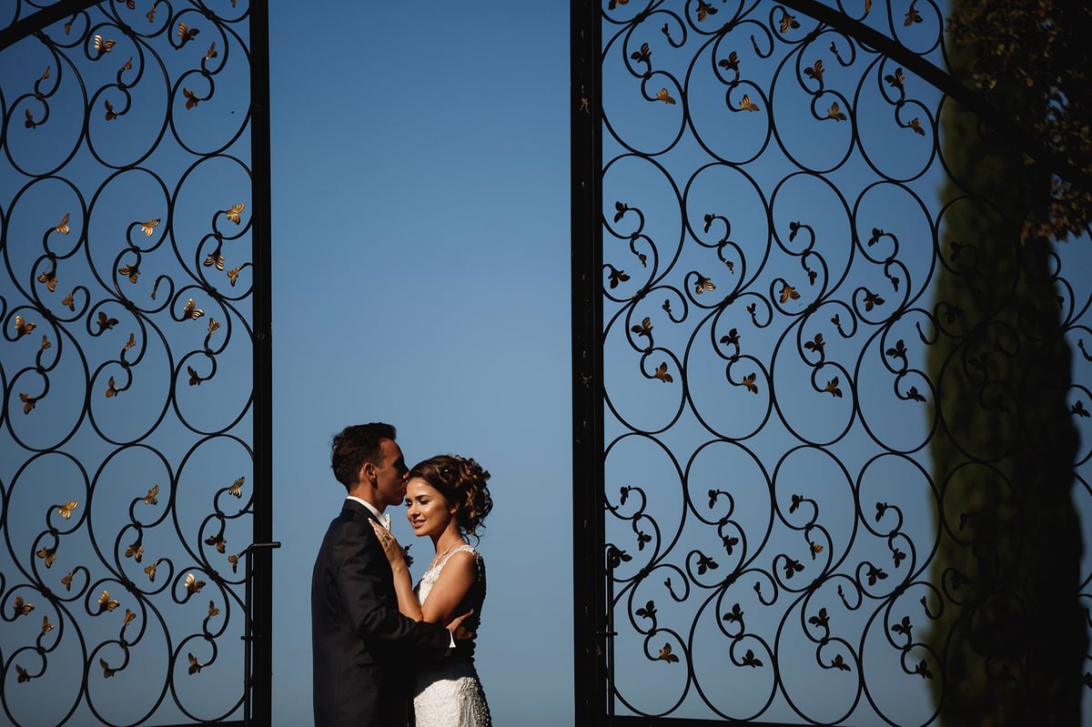 Bride and groom kissing between ornate metal gates, Tanzania elopement photographer capturing a romantic wedding moment against blue sky