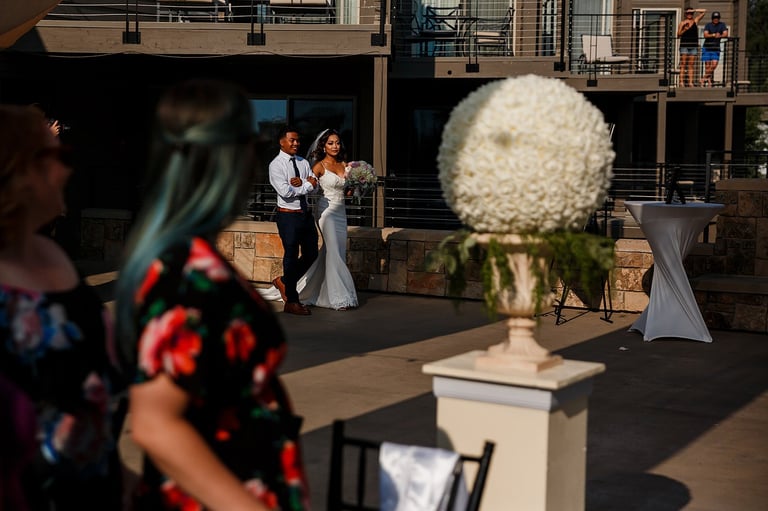 Wedding ceremony with bride and groom dancing outdoors while guests watch, white floral arrangement in foreground