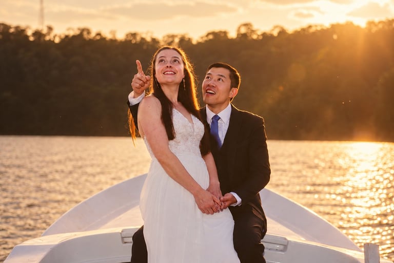 Bride and groom on a boat at sunset, holding hands and looking upward together