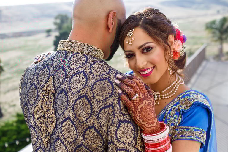 Bride and groom in traditional Indian wedding attire embracing outdoors with scenic landscape background