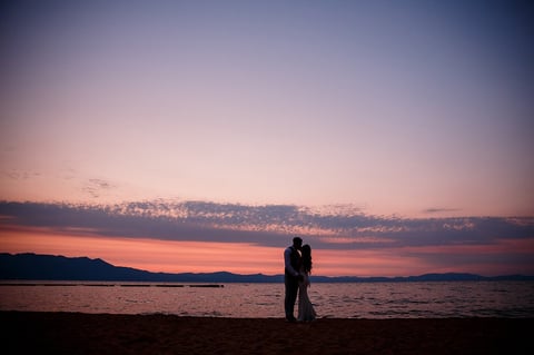 Silhouetted couple standing on beach at sunset with mountains in background