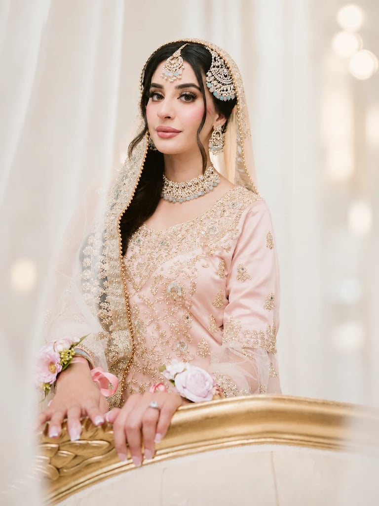 Bride wearing ornate beaded blush pink gown with embellished veil, jewelry and flower bouquet