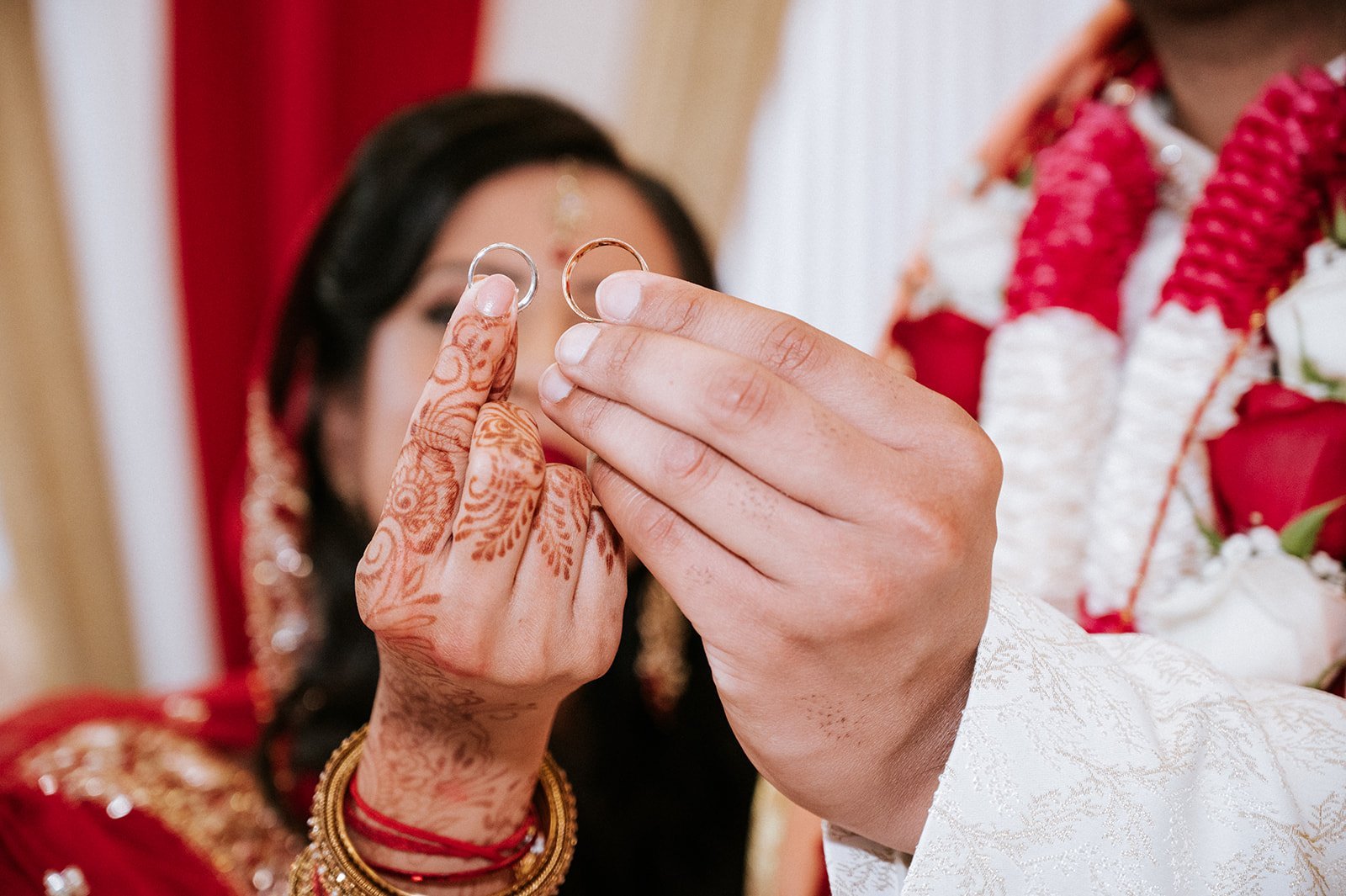 Bride and groom displaying their hands with wedding rings and henna during traditional wedding ceremony