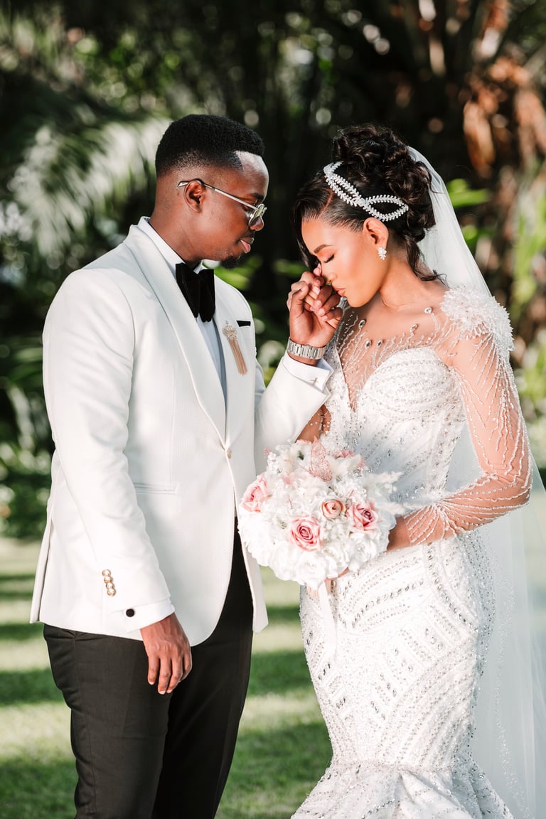 Bride and groom in formal wedding attire sharing an intimate moment in a garden setting, bride holding a white and pink bouquet — best wedding photographer Tanzania Dar es Salaam by Royal Wedding Cinema & Photography