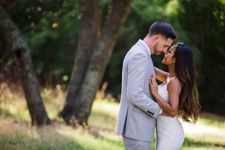 Couple in wedding attire kissing outdoors under trees in natural daylight setting
