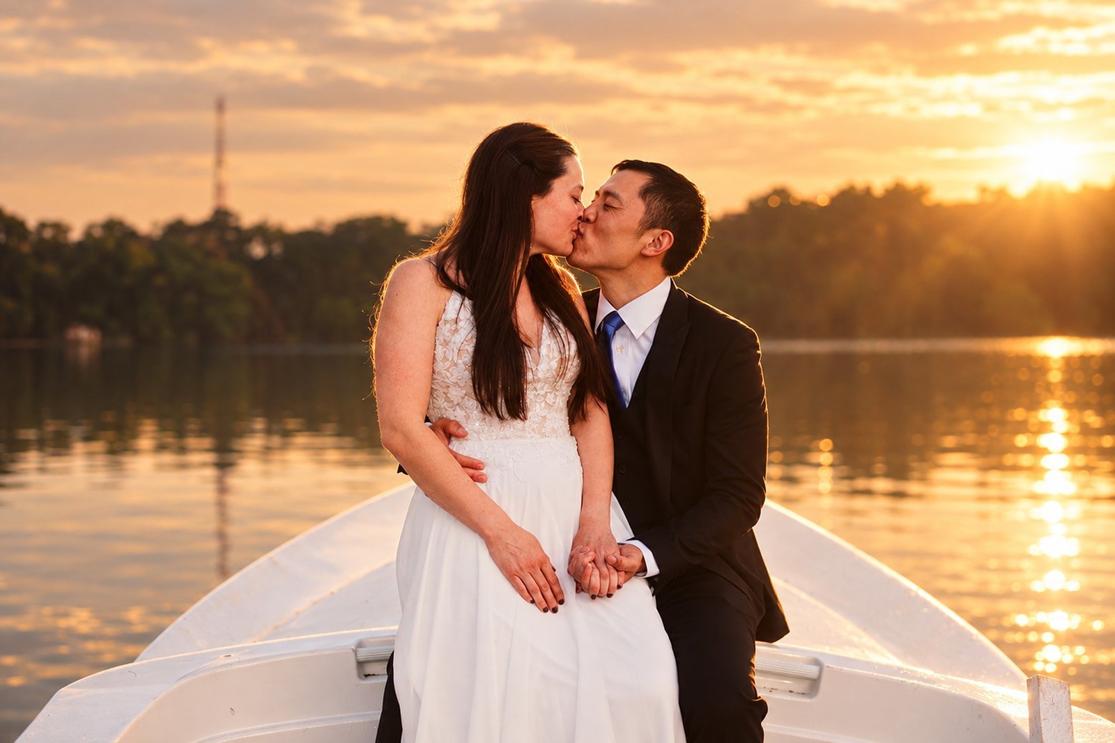 Newlywed couple kissing on a boat at sunset with golden hour light reflecting off calm water
