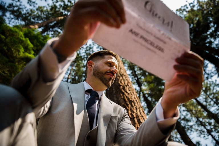Groom in beige suit reading wedding certificate outdoors, creative couple session during reception