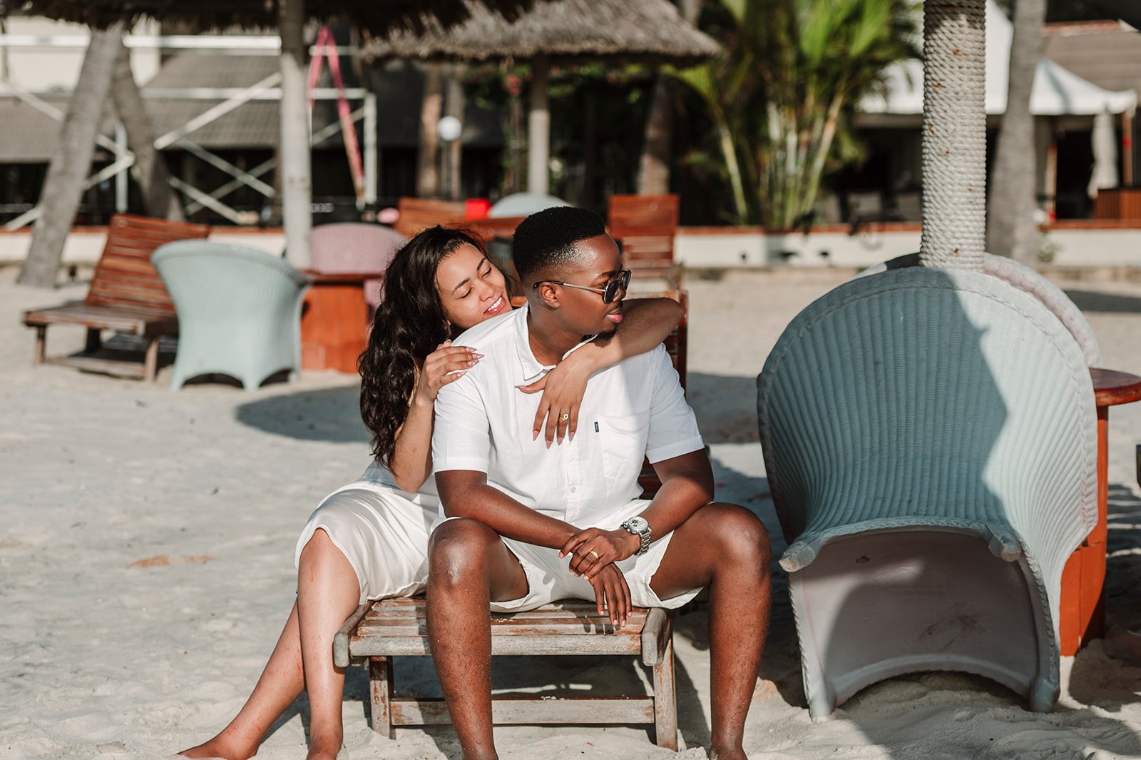 Couple sitting together on a beach lounge chair in white casual clothing at a tropical resort