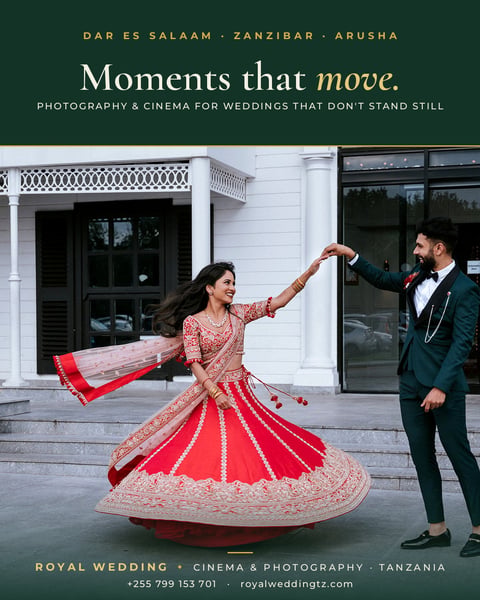 Bride in red and gold lehenga twirling with groom in dark suit outside white colonial building, wedding photography portfolio image