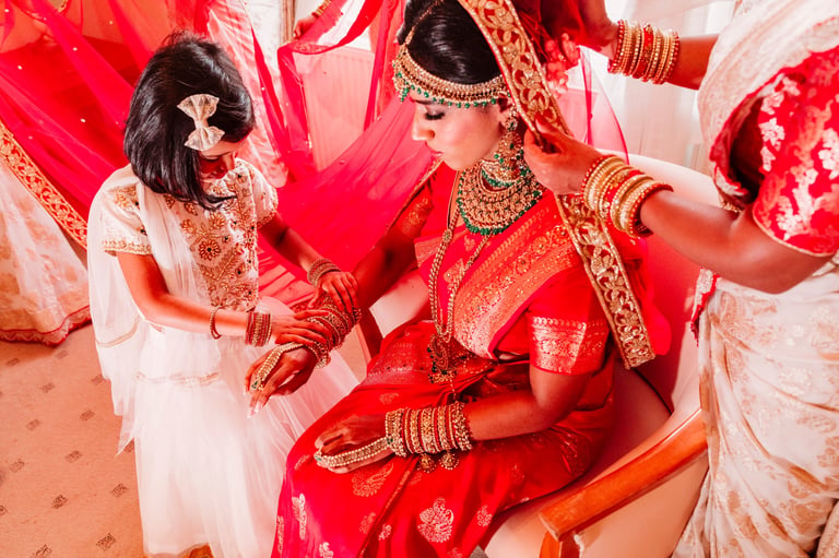 Bride in red traditional wedding dress with gold jewelry being prepared by bridesmaids in white during Indian wedding ceremony — Asian wedding photographer Tanzania Dar es Salaam by Royal Wedding Cinema & Photography