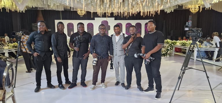 Group of men in formal attire standing in an elegant event space with chandeliers and floral decorations