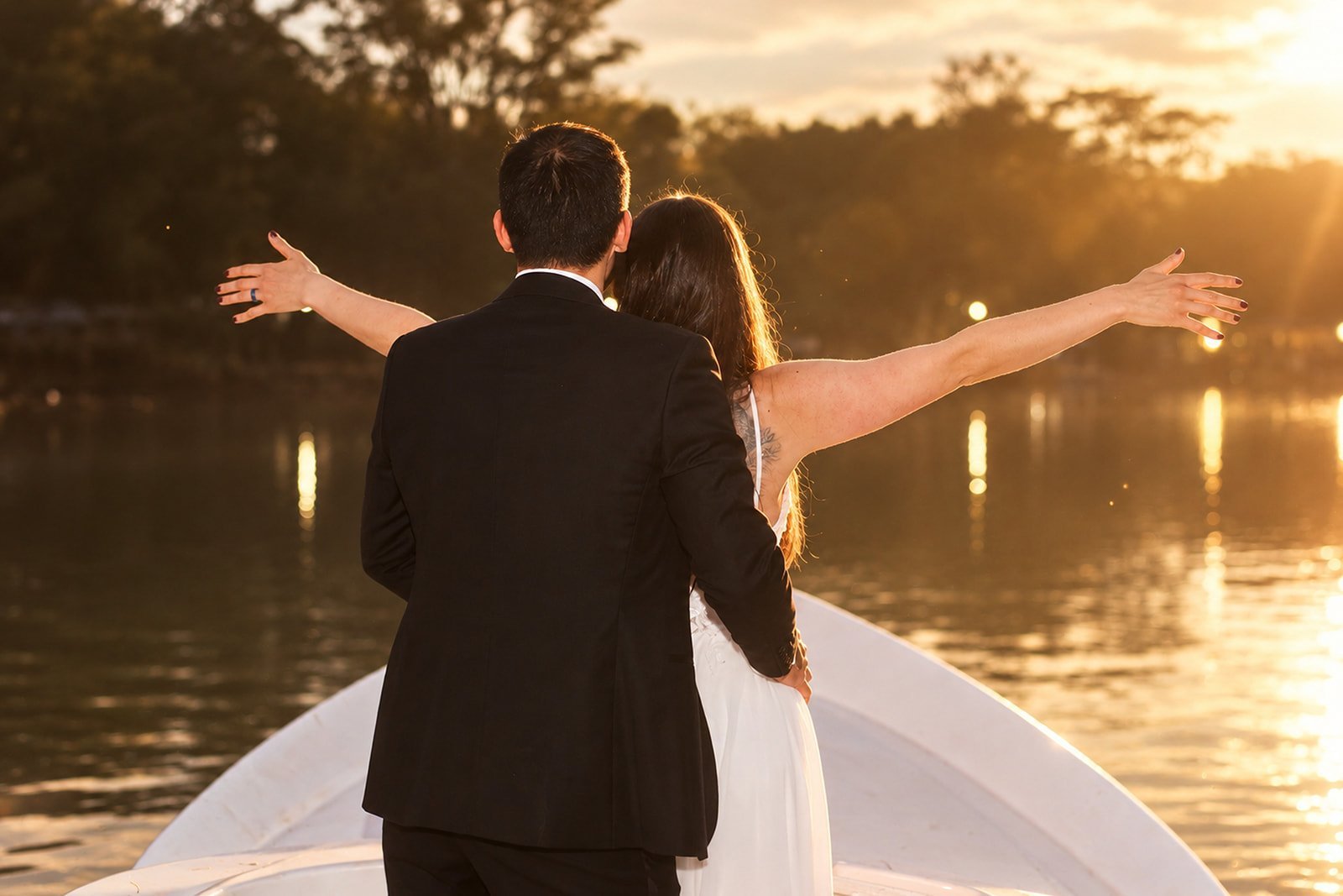 Newlyweds in a boat with arms spread wide, celebrating at sunset over a calm river
