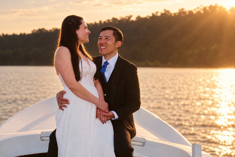 Bride and groom smiling together on a boat at sunset over a lake with forested shore in background