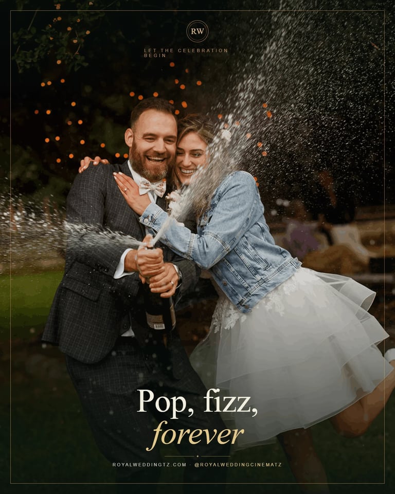 Couple celebrating with champagne spray groom in gray suit bride in white dress and denim jacket Zanzibar wedding celebration