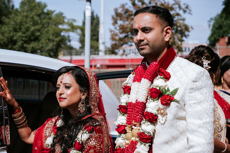 Bride and groom in traditional Indian wedding attire with red and white floral garlands and ornate clothing
