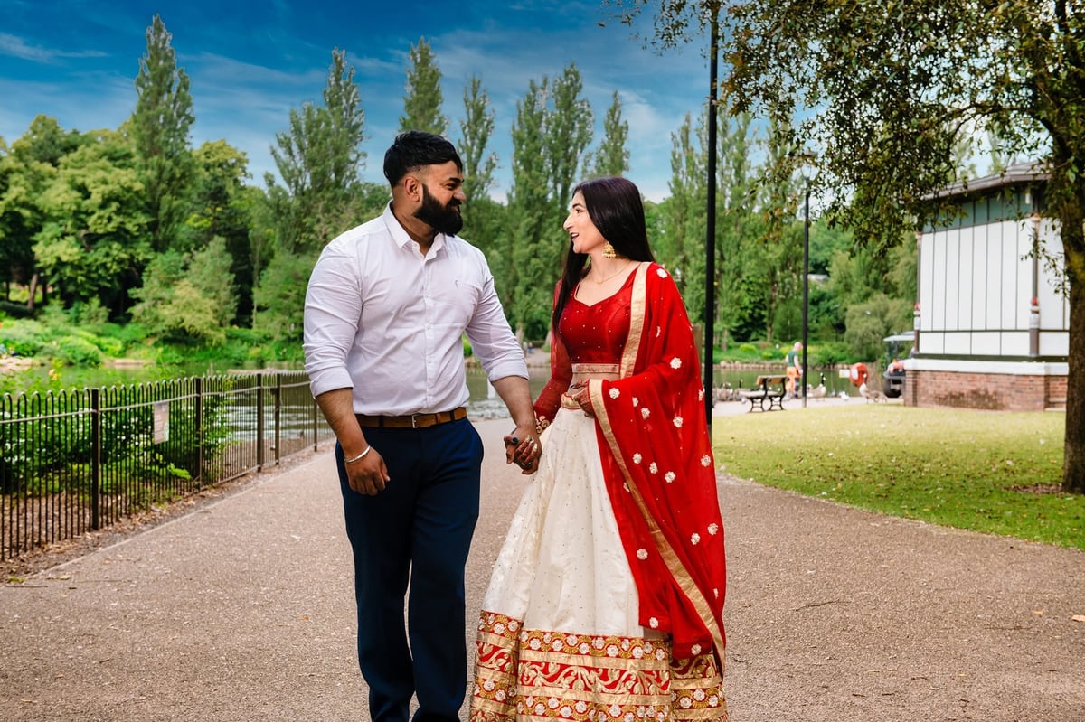 Couple walking hand in hand on a park path, destination wedding Tanzania with bride in red traditional dress and groom in light shirt