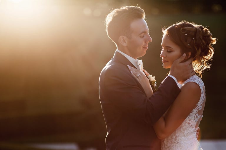 Bride and groom embracing at sunset with golden light, dressed in wedding attire
