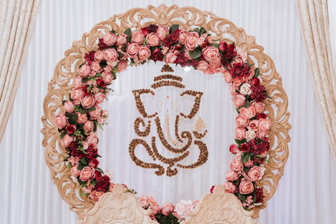 Ornate floral arch with pink and red roses surrounding a gold Ganesha symbol on white backdrop