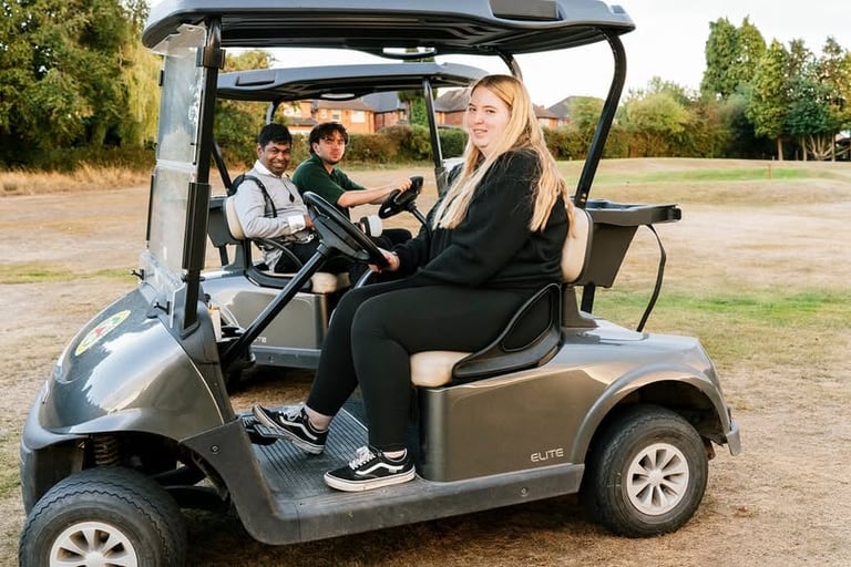 Woman and two children sitting in a golf cart on a paved area with trees in the background