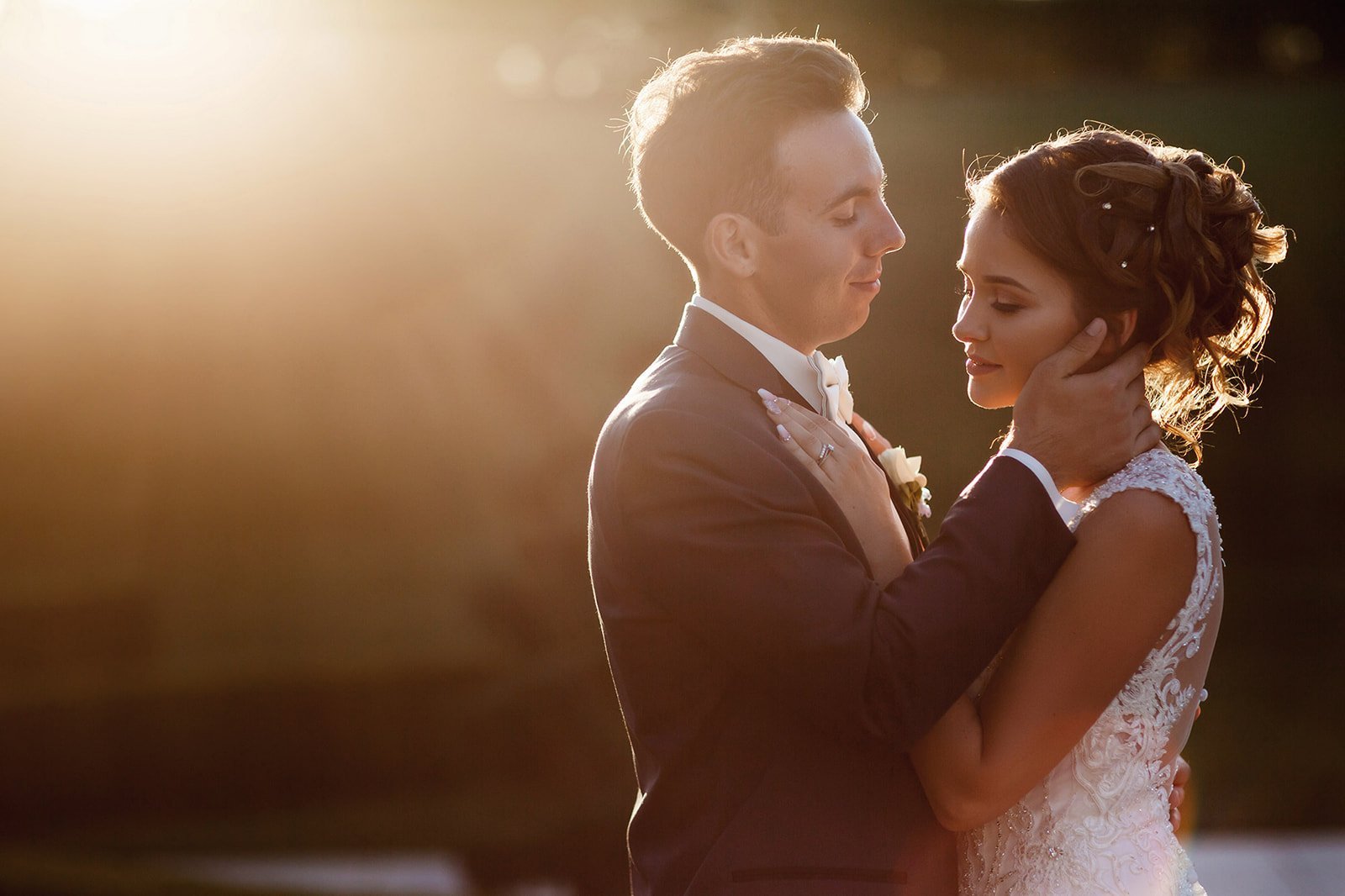Bride and groom embracing during sunset with golden backlighting on their wedding day