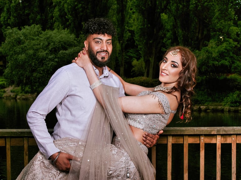 Bride and groom posing together on a wooden deck by a lake with green trees in background