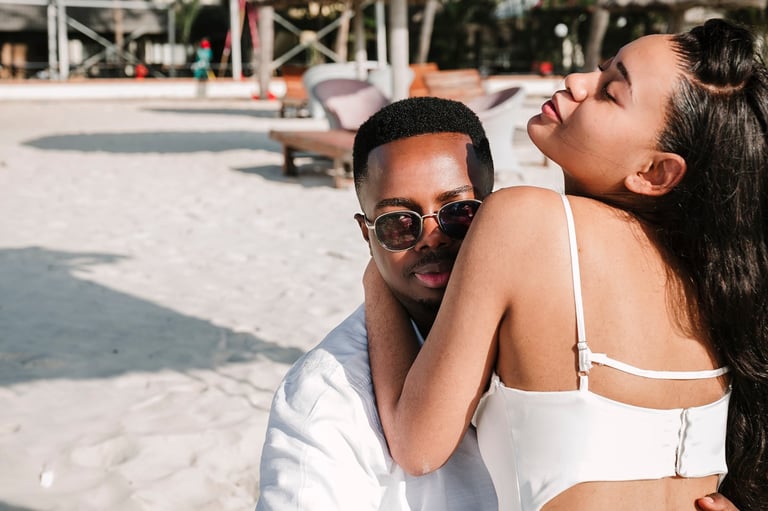 Two people smiling together on a sunny beach with palm trees and loungers in the background