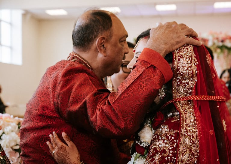 Groom in red traditional attire kissing bride wearing red embellished wedding dress at indoor ceremony