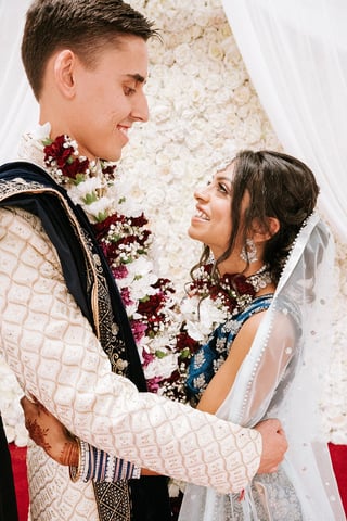 Hindu bride and groom in traditional Indian wedding attire smiling at each other in front of white floral backdrop — Hindu wedding photography & videography Dar es Salaam Tanzania