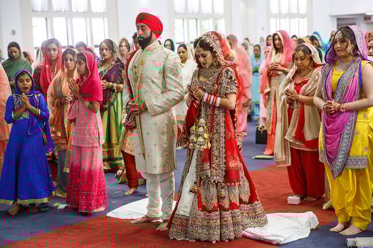 Indian wedding ceremony with bride in red embroidered lehenga and groom in cream sherwani performing rituals surrounded by guests in colorful traditional attire