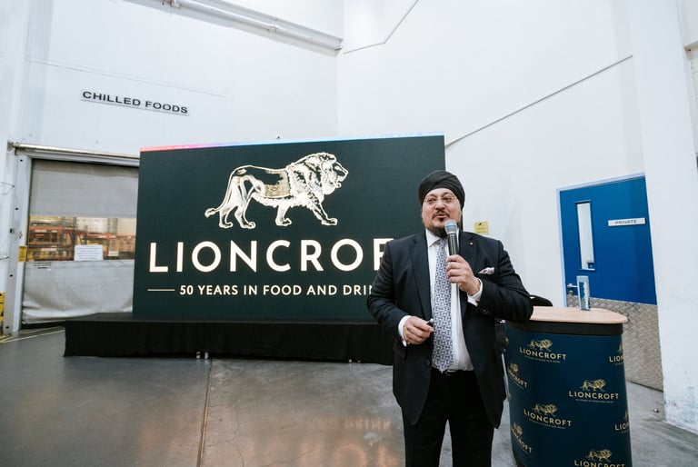 Corporate brand event photography — business executive speaking at Lioncroft food and drink company event with promotional signage, Royal Wedding Cinema Tanzania